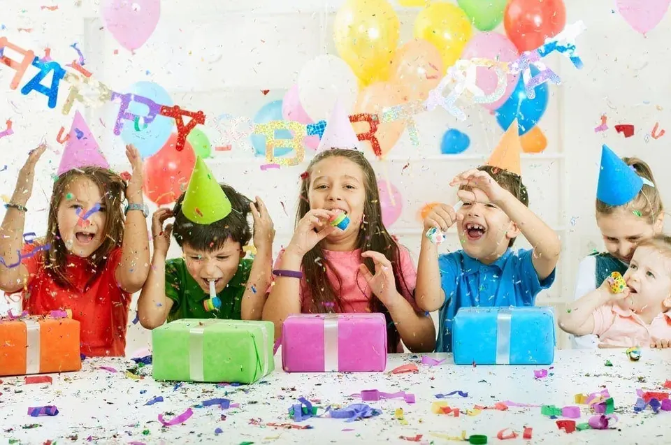 Kinder mit bunten Partyhüten feiern ausgelassen mit Konfetti, Luftballons und Geschenken